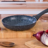 Black non-stick frying pan with speckled finish on wooden kitchen counter