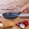 Black non-stick frying pan with speckled finish held by handle, shown in kitchen setting