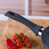 Black non-stick frying pan handle close-up with fresh tomatoes and red chilli on wooden board