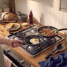 Frying pans on hob with cooked egg, sausages, and mushrooms for breakfast scene