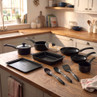 8-piece black non-stick cookware set with utensils on kitchen counter