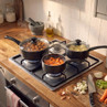 Set of three black saucepans with glass lids cooking vegetables on gas hob in kitchen