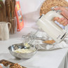 Cream hand mixer in use mixing batter in a bowl on a kitchen worktop