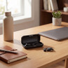 Black wireless earbuds with open charging case on desk, two earbuds placed nearby.