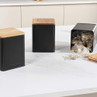 Set of three black storage canisters with wooden lids, one open with tea bags inside
