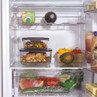Fridge shelf with glass food containers, fresh vegetables and drinks visible