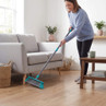 Woman sweeping wooden floor with grey broom in living room