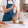 Hand blender set blending tomato sauce, extra attachments and chopped vegetables on kitchen counter