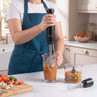 Hand blender in use with mixing jug, chopping bowl, and whisk attachments on kitchen counter