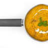 Stainless steel saucepan filled with carrot soup, garnished with cream and basil