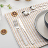 Four-piece stainless steel cutlery set displayed on striped napkin with plate and glass