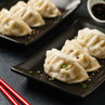 Three steamed dumplings on a black plate, garnished with sesame and spring onion.