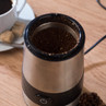 Silver electric coffee grinder with ground coffee, shown on kitchen worktop