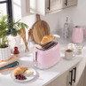 Pink two-slice toaster warming croissants on kitchen worktop, matching kettle in background