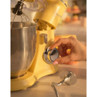 Close up of yellow stand mixer with metal bowl, hand turning speed dial.