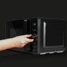 Black microwave oven with digital display, shown as a hand adjusts the control dial.