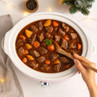Slow cooker with beef stew, carrots and potatoes being stirred by hand