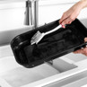 Hand washing a large black roasting tray in a kitchen sink with a cleaning brush