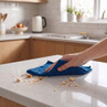 Hand wiping crumbs from kitchen worktop with blue microfibre cloth