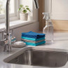 Stack of blue and grey cleaning cloths beside sink with spray bottle