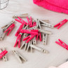Pack of pink and grey plastic clothes pegs for laundry, shown on a surface.