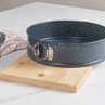Round, blue speckled springform cake tin shown on wooden board