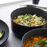 Black non-stick saucepan with creamy pasta and herbs, shown on kitchen worktop