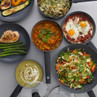 Assorted meals served in grey non-stick pans, showing pasta, curry, eggs, stir fry and soup.
