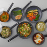 Set of non-stick frying pans with assorted cooked meals and vegetables, top view