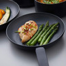 Non-stick frying pan with cooked chicken breast, asparagus, and garnished vegetables.