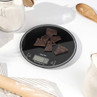 Digital kitchen scale with dark chocolate pieces on top, black glass surface, baking context