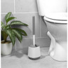 Grey and white toilet brush with holder on tiled bathroom floor next to toilet