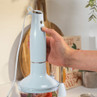 Hand holding light blue hand blender blending fruit in a container on kitchen worktop