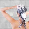 Person washing hair with shampoo under shower, white tiled background