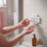 White wall-mounted silicone body scrubber in use in shower