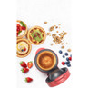 Red pie maker on white surface with filled pastry bowls and fresh fruit, breakfast setting