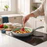 Non-stick frying pan with green interior on induction hob, cooking scrambled eggs and vegetables