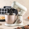 Cream stand mixer with stainless steel bowl on kitchen counter, baking in progress