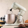 Cream stand mixer with metal bowl on kitchen counter, surrounded by baking pastries.