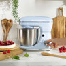 Light blue stand mixer with stainless steel bowl on kitchen counter, hand turning dial
