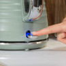 Sage green electric kettle being switched on, showing blue power light.