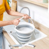 Collapsible grey and white bucket with soap suds held over kitchen sink
