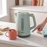 Green electric kettle on countertop, being switched on, next to mug with tea bag