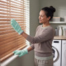 Pair of light blue cleaning gloves wiping wooden window blinds in laundry room