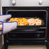 Tray of oven chips and onion rings being placed in oven with oven gloves