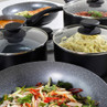 Set of black non-stick saucepans and frying pans with glass lids shown in use