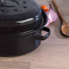 Black speckled roasting pan on worktop with onion, tomatoes and wooden spoon in background