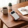 Grey portable power bank with digital display held in hand on desk