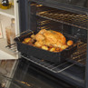 Black roasting tin with golden roast chicken and potatoes in an open oven