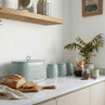 Set of green kitchen storage canisters and bread bin on worktop, sliced loaf, modern style